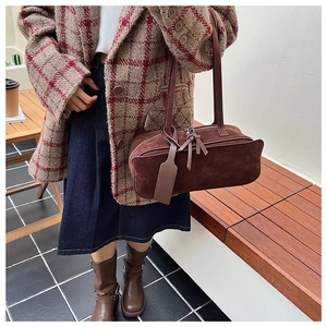 Close-up of brown suede pillow bag featuring double zippers and long leather tassels