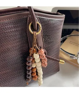 Detail of wooden beaded charm with metal ring on a brown woven texture tote bag
