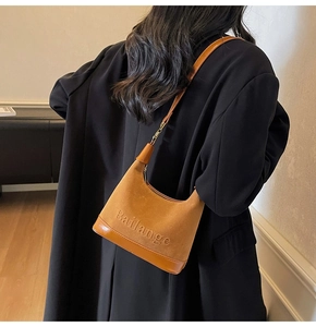 Détail de la texture suède marron caramel et logo embossé sur le sac à bandoulière
