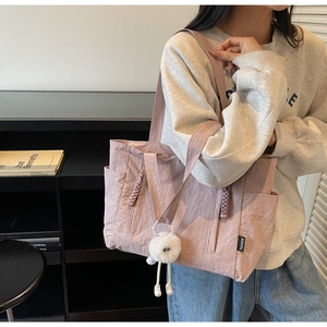 Detail of mauve nylon tote bag with plush pompom and black fashion label on the front