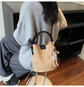 Detail showing matte camel bucket bag with black handles and cute plush rabbit charm