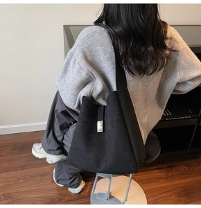 Model wearing black suede shoulder bucket bag with silver metal buckle detail