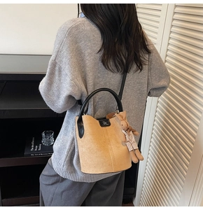 Detail of camel suede bucket bag with black handles and cute rabbit charm on a model
