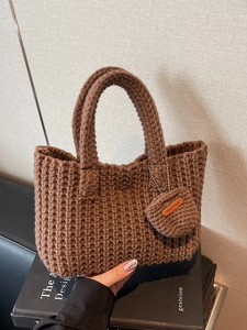 Brown handmade chunky knit tote bag with dual handles and round charm on leather base