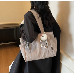 Detail of nylon tote bag with fashion label and white monster plush charm accessory