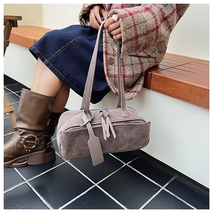 Close-up of matte suede shoulder bag with dual tassel zippers and decorative hangtag