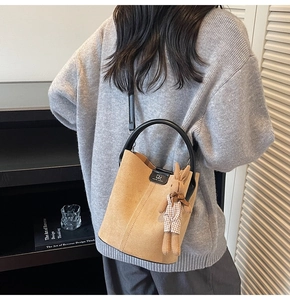 Brown suede bucket bag with stylish rabbit charm and black handle shown in a home setting
