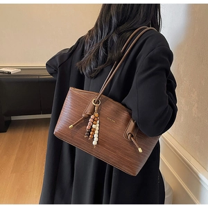 Close-up of brown woven leather tote bag with unique ethnic beaded charm and slim strap