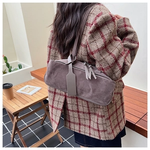 Grey suede pillow bag with fringe zipper detail worn by model in casual outdoor setting