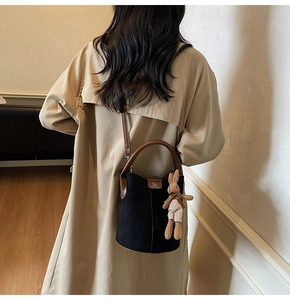Crossbody shot of a black matte bucket bag with brown straps and cute rabbit charm