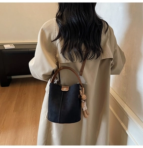 Matte black bucket bag with brown handles and a cute rabbit charm on a beige trench coat