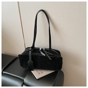 Detail view of black suede shoulder bag with dual zippers and leather tassel on a desk