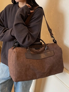 Brown suede travel duffel bag with leather trim and shoulder strap shown in use