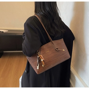 Detail view of brown woven tote bag with beaded charm and slim shoulder straps