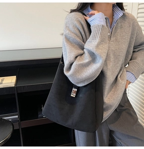 Detail of black suede tote bag with silver metal buckle on minimalist grey sweater