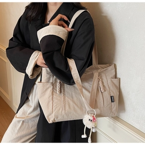 Detail of beige nylon tote bag with plush charm and fashion tag worn by model