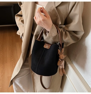 Detail of black matte bucket bag with brown leather strap and a cute rabbit charm