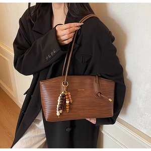 Detail of a brown woven texture tote bag with a beaded tassel and golden zipper