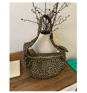 Detailed view of leopard print canvas crescent bag with metal zipper on a rustic wooden desk