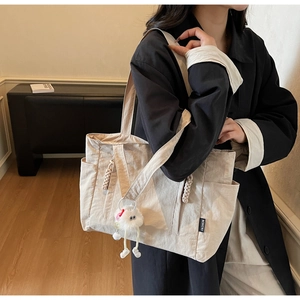 Detail of light beige nylon tote bag with side pocket and cute plush pendant charm