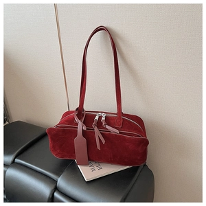Detail of burgundy velvet underarm bag with double zippers on a leather stool