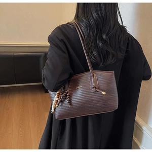 Detailed close-up of dark brown woven leather tote bag with elegant beaded charm accessory