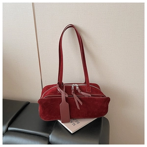 Detailed shot of dark red suede boston bag with zipper and leather tag on a black seat