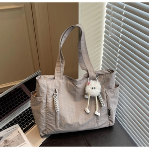 Detail of taupe nylon tote bag with plush charm and organized side storage pockets