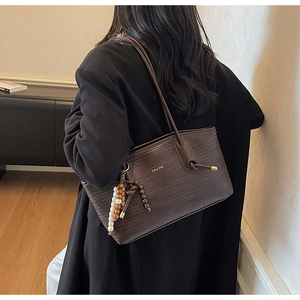 Detail of dark brown woven tote bag with gold logo and wooden beaded tassel charm