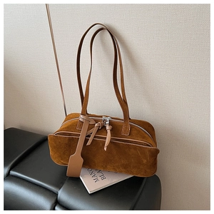 Close-up of brown suede pillow bag with long leather zipper pulls and minimalist tag