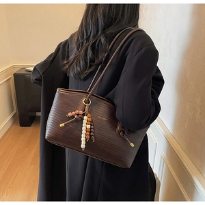 Detailed side view of dark brown woven leather tote bag with stylish beaded tassel charm