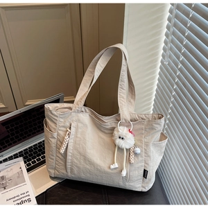 Close-up of beige nylon tote bag with multi-pocket design and decorative plush pompom charm