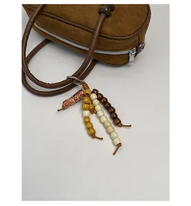 Dettaglio di un ciondolo in perline di legno su una borsa Boston in camoscio marrone