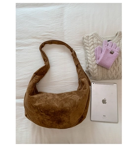 Dettaglio flat lay di una grande borsa hobo in pelle scamosciata marrone su biancheria