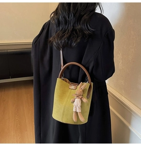 Detail of green frosted bucket bag with brown leather handles and a plush bunny charm