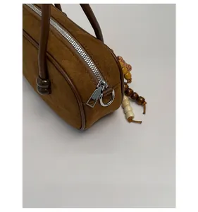 Dettaglio di borsa bowling in camoscio marrone con zip argento e ciondolo in legno