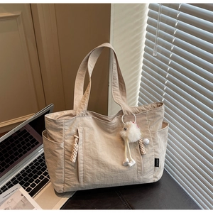 Detail of beige nylon tote bag with zipper pocket and cute white plush monster charm