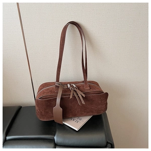 Detail of vintage dark brown suede pillow bag with fringe zipper and leather tag on books