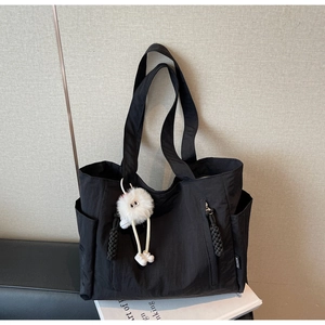 Detailed view of black nylon tote bag with side pockets and a white plush toy charm