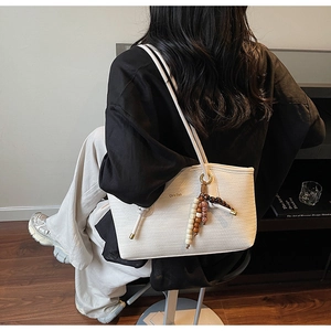 Close-up of white woven shoulder bag with beaded fringe tassel and gold brand logo
