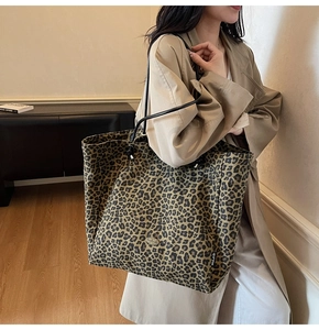 Detailed shoulder view of a large leopard print tote bag with leather straps and logo plaque