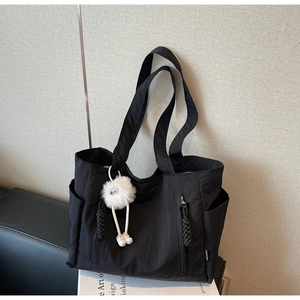 Detail view of large nylon tote bag with plush monster charm and side pockets