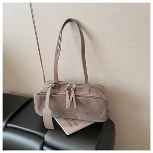 Close-up of brown suede pillow bag with fringe zipper detail on a black leather bench