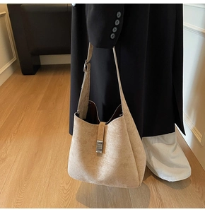 Detail view of khaki suede hobo bag with silver buckle worn by a model in black coat