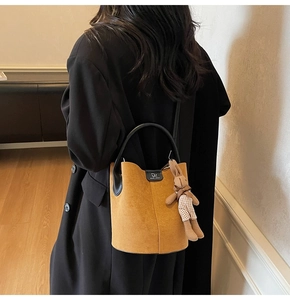 Detail of mustard yellow suede bucket bag with check rabbit pendant and black handle