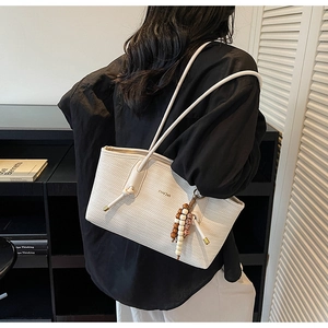 Detailed view of white woven shoulder tote bag with a wooden bead charm detail