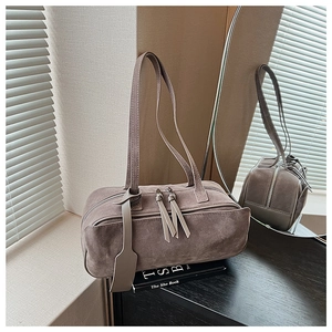 Detail of taupe suede pillow bag with dual zippers and decorative hangtag on mirror