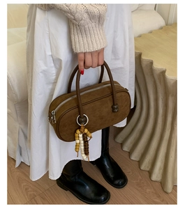 Dettaglio borsa Boston in camoscio marrone con ciondolo di perline tenuta da modella