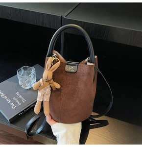 Detail of a dark brown suede bucket bag featuring a cute rabbit charm and top handle