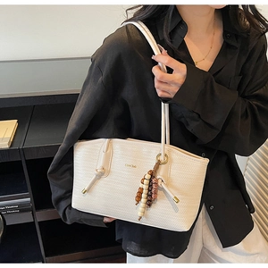 Detail of off-white woven tote bag with golden logo and ethnic wood bead charm